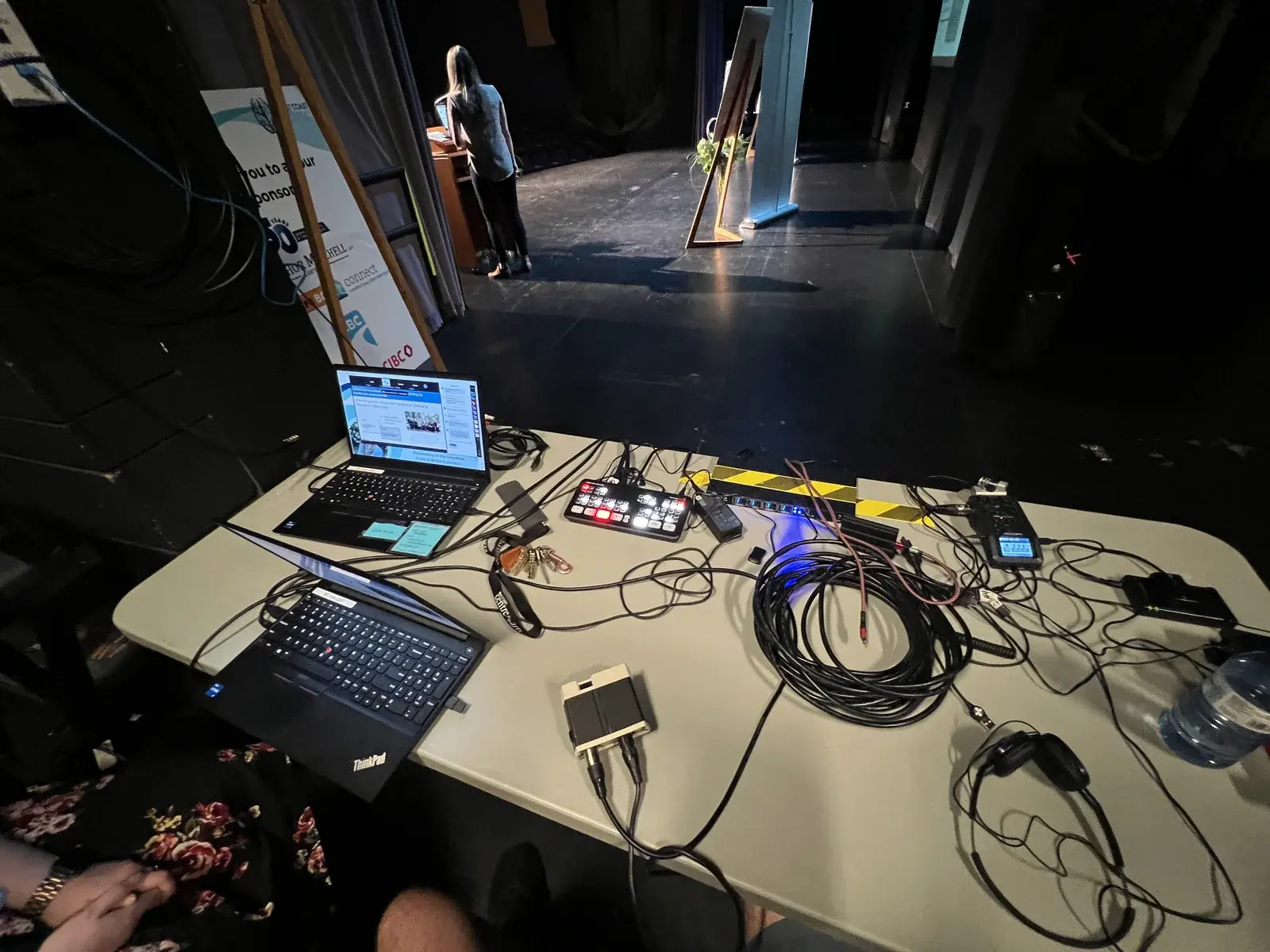 Livestream production table with laptops, switching and cables beside a conference stage